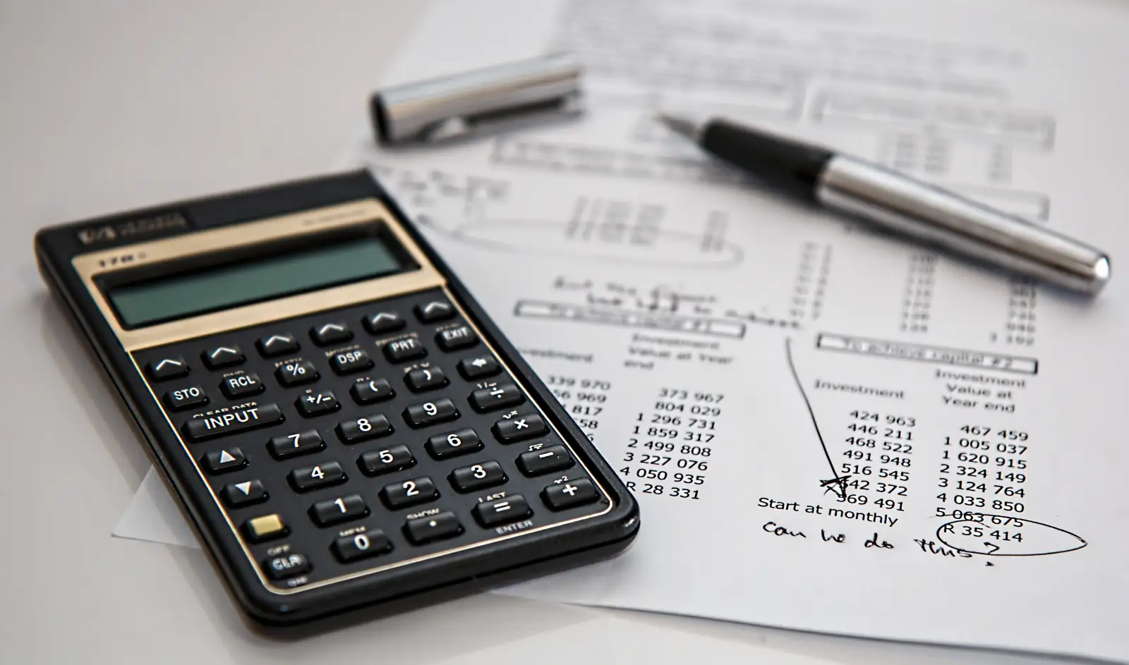 A desktop calculator and a pen lying on printed forms with columns of figures